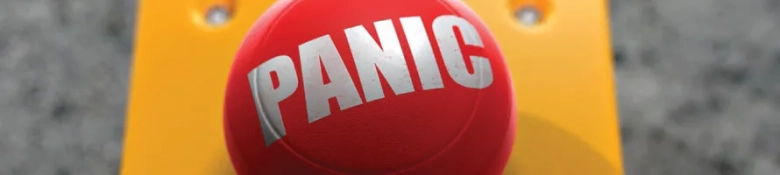 Red panic button with the word "PANIC" in capital letters, mounted on a yellow surface with a blurred background.