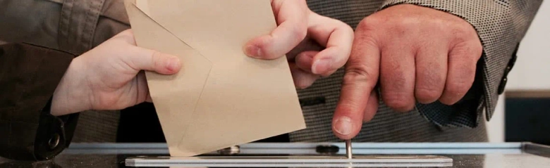 Close-up of a person casting a ballot in a voting box, symbolizing civic duty and local government participation.