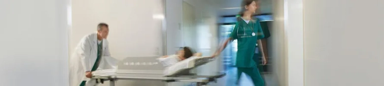 Blurred motion of a student nurse walking briskly in a hospital corridor with a doctor pushing a patient on a stretcher.