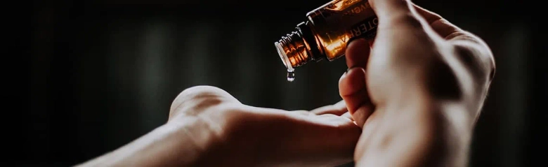 Close-up of hands dispensing essential oil from a dropper bottle.