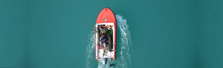 Aerial view of a fisheries enforcement officer piloting a red boat on a turquoise sea.
