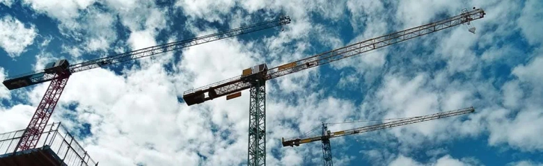 Tower cranes against a cloudy sky at a construction site.