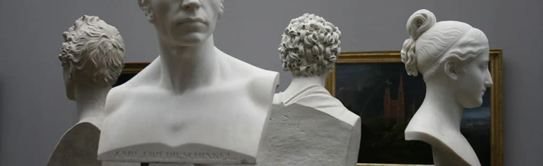 Busts of classical sculptures on display with a framed artwork in the background, showcasing exhibition design.