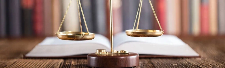 Scales of justice on a wooden surface with an open book in the background.