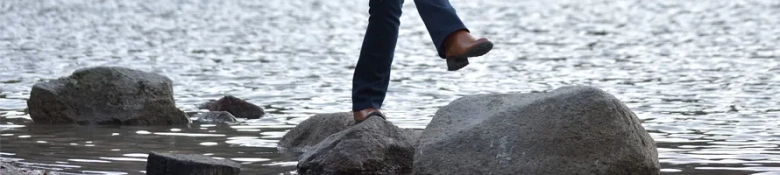 Person stepping across stones in water, symbolizing progression or careful navigation.