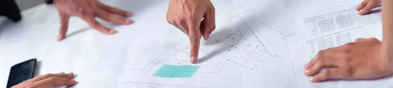 Close-up of hands pointing and discussing over architectural blueprints on a table.