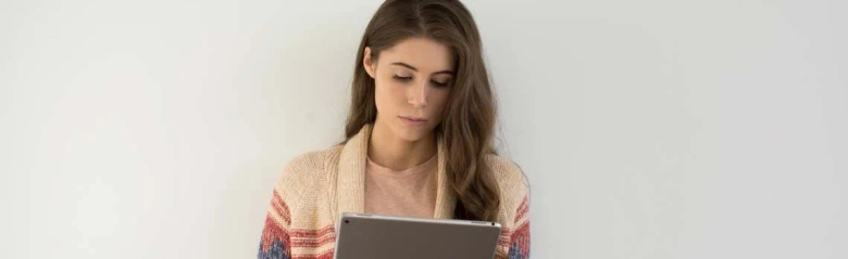 A woman looking down at the screen on an electronic device that she's holding.