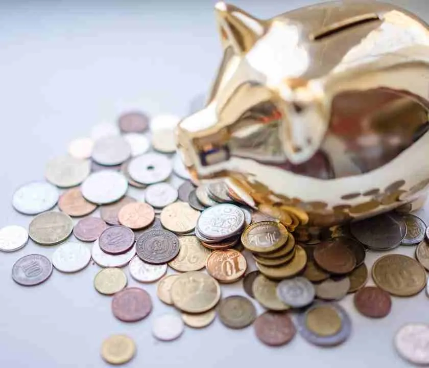 A golden piggybank with coins spread out around it