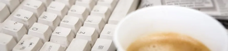 Close-up of a white keyboard with a coffee cup on a desk, suggesting a journalist's workspace.