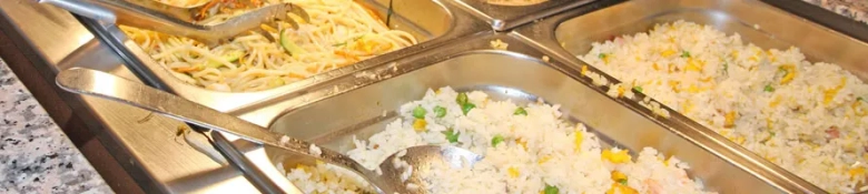 Stainless steel serving trays with pasta, white rice, and fried rice in a buffet setup.