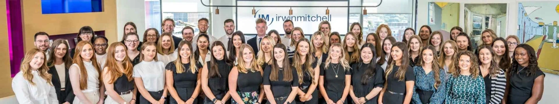 Group photo of Irwin Mitchell employees in office setting with company logo in the background.