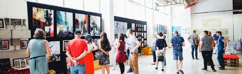 Visitors viewing artwork at an exhibition with various pieces displayed on panels and tables.