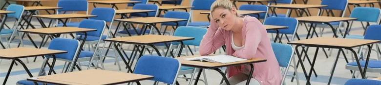 Stressed student sitting alone in an exam hall with her head resting on her hand looking away from her paper.