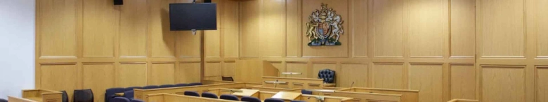 Interior of a moot court room at Nottingham Law School with wooden panels and the Royal Coat of Arms on the wall.