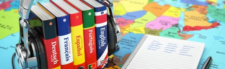 Stack of language learning books with headphones and a notepad on a world map background.