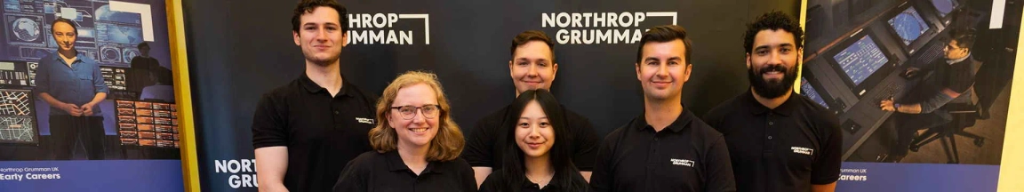 Group of Northrop Grumman employees smiling in front of a company banner at a career event.