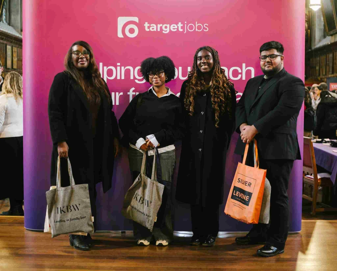 Group of 4 women with black hair holding merchandise tote bags from pupillage fair, infront of targetjobs banner reading 'targetjobs: Helping you reach your full potential'