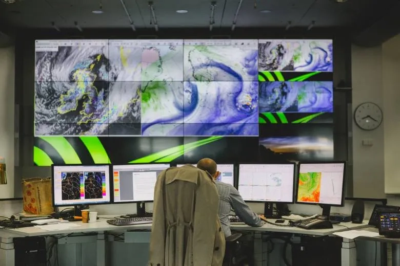 A man sat infront of a bank of computer screens with weather patterns on 