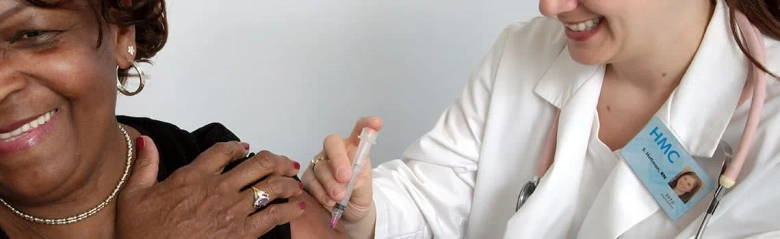 Health visitor administering a vaccine to a smiling elderly woman.