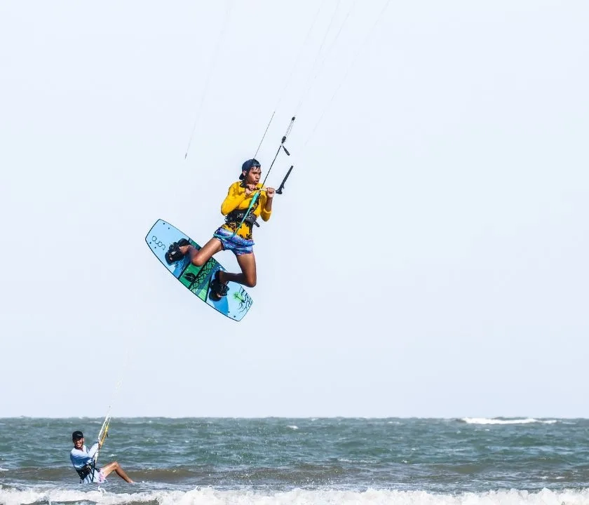 A man wakeboarding. He is jumping in the air. There is another wakeboarder in the water. 