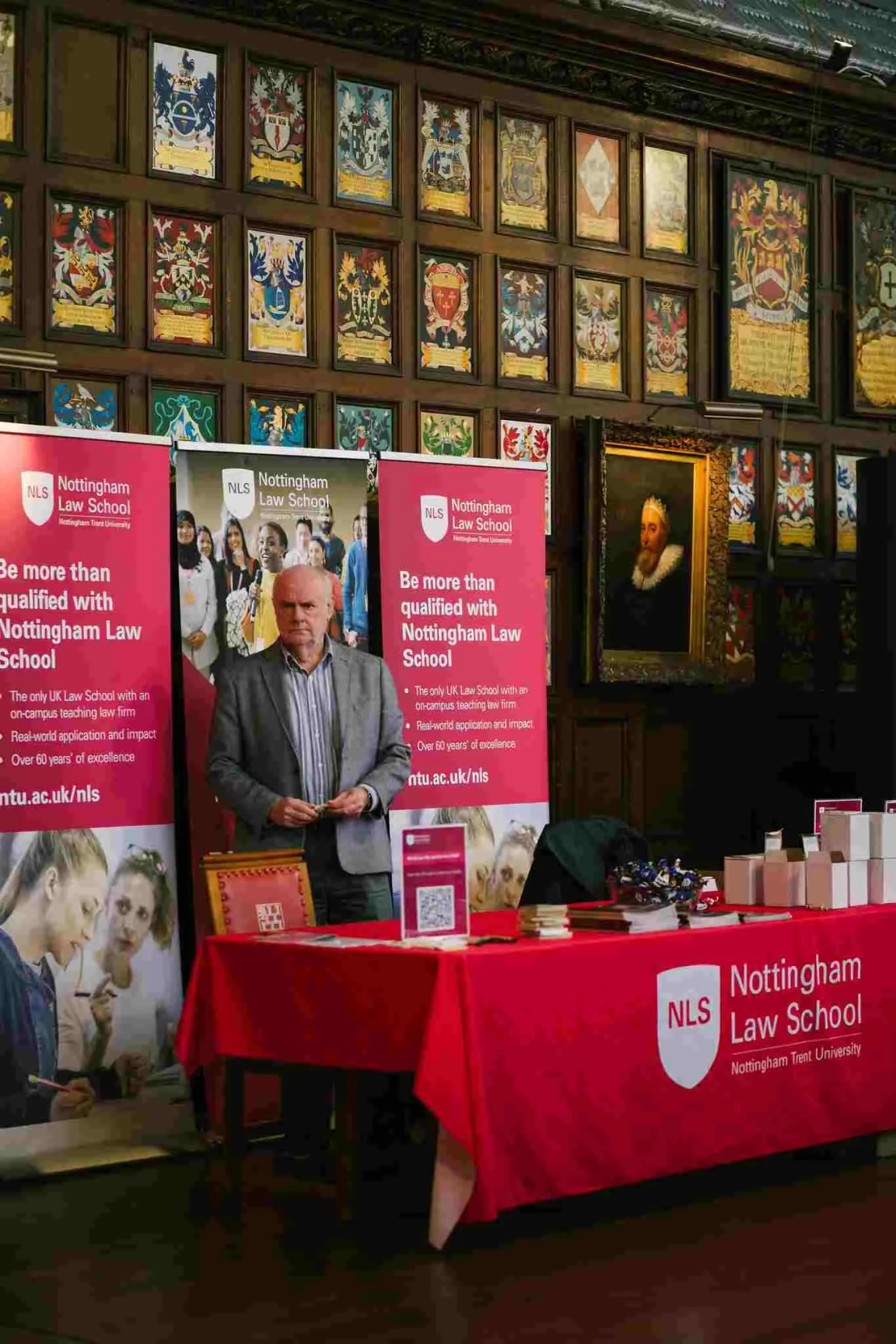 Man with grey hair stood at exhibitor stand covered in red tablecloth and chamber merchandise