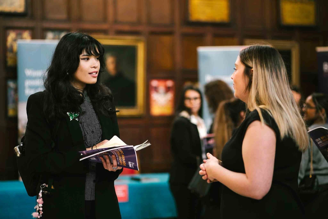 Student with black hair holding pupillage guide, speaking to female chamber representative with blonde highlights