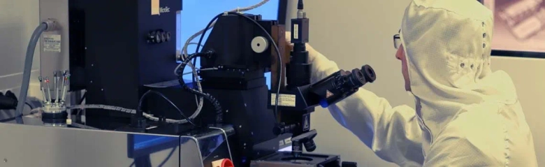 Scientist in a clean suit using a microscope in a nanotechnology lab.