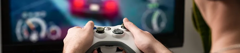 Close-up of hands holding a game controller with a blurred video game screen in the background.