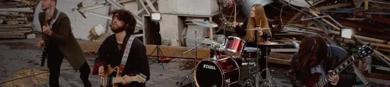 Band performing with a guitarist, bassist, drummer, and another guitarist amidst a backdrop of debris.