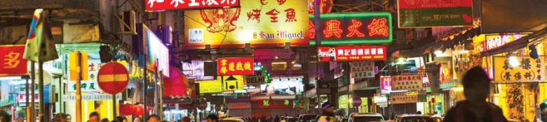 Bustling street scene at night with illuminated signs in various languages.
