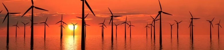 Sunset over ocean with silhouette of offshore wind turbines.