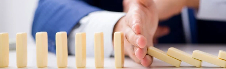 Person stopping a row of dominos from falling to represent risk management concept.