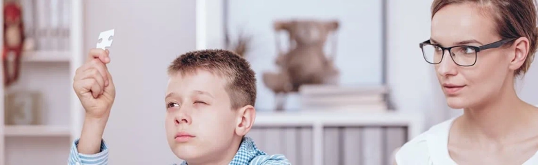 Child looking at a puzzle piece with a focused expression while a psychotherapist observes him.