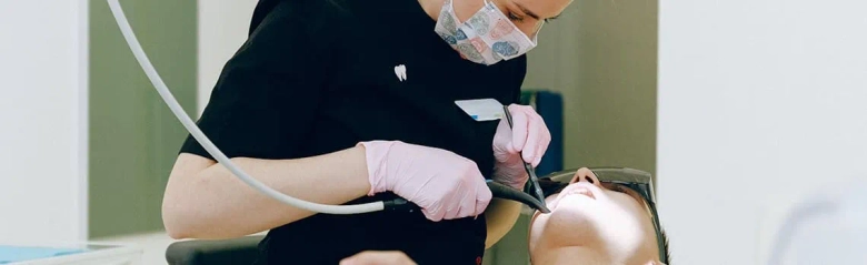 Dental hygienist wearing a mask and gloves while cleaning a patient's teeth with dental instruments.
