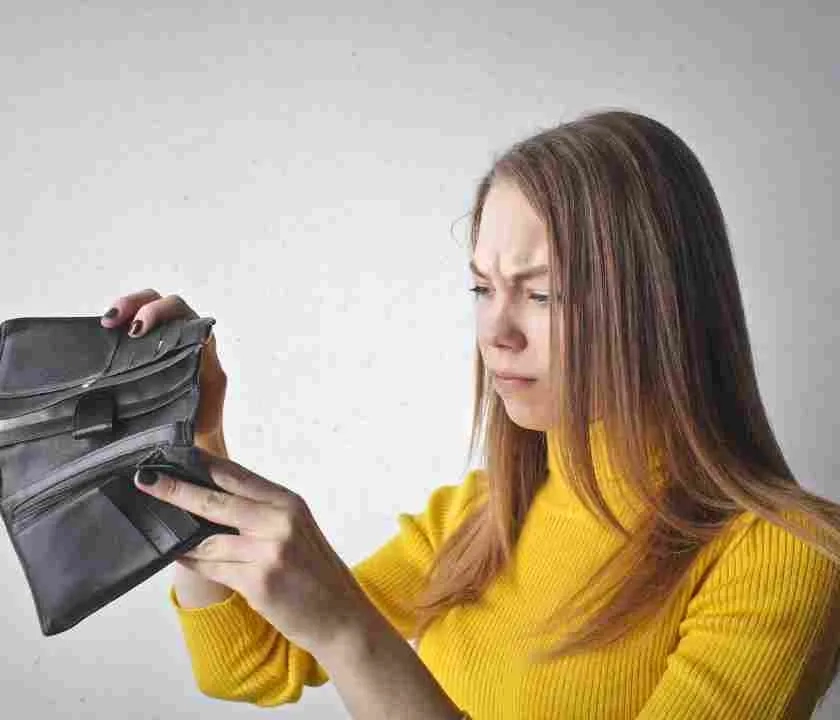 A woman holding up an empty wallet, looking disgusted