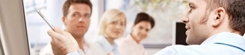 Group of professionals in a meeting with one person presenting ideas on a whiteboard.