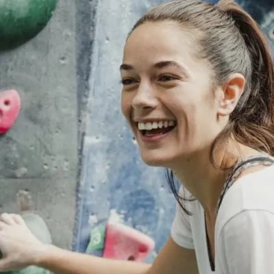 a woman smiling at a climbing wall 