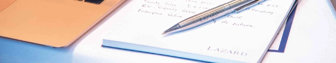 Close-up of a notepad with handwritten notes and a pen, with the word "LAZARD" visible on the page.