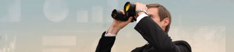 Man in a suit looking through binoculars, symbolizing the search for job opportunities.