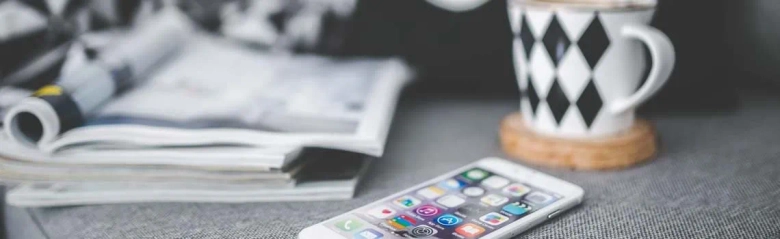 a pad of paper and coffee mug in the background and a mobile phone in the foreground all atop a media planner's desk.