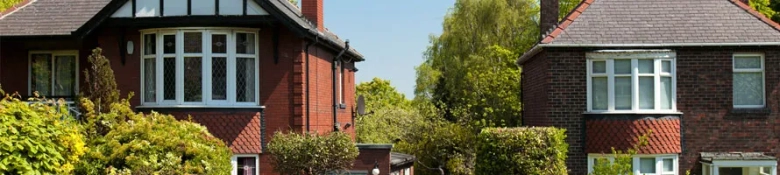 Row of traditional red brick houses with greenery under a clear blue sky.