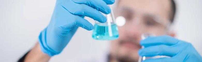 Scientist in lab coat examining a test tube with blue liquid, representing work in immunology.
