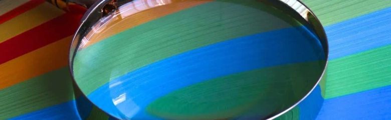 Close-up of a magnifying glass inspecting the surface of colorful striped material, symbolizing quality inspection.