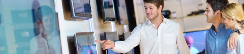 Young retail employee assisting customers with electronic product choices in a store.