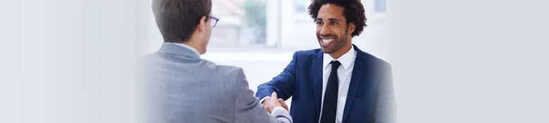 Two professionals shaking hands in an office environment, one facing the camera with a smile.
