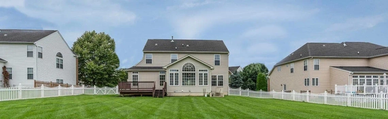 Suburban backyard with a well-maintained lawn and a two-story house with a wooden deck.