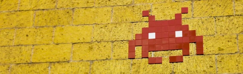A character from the video game Space Invaders painted in red on a yellow brick wall.
