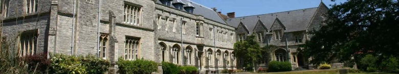 Panoramic view of the University of Chichester's historic stone building with arched windows surrounded by greenery.