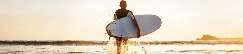 A surfer walking wading out into the sea carrying their surf board. 