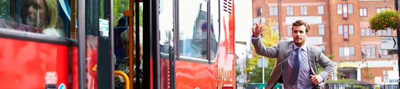 Man in a suit running after a bus, waving his hand to catch it.